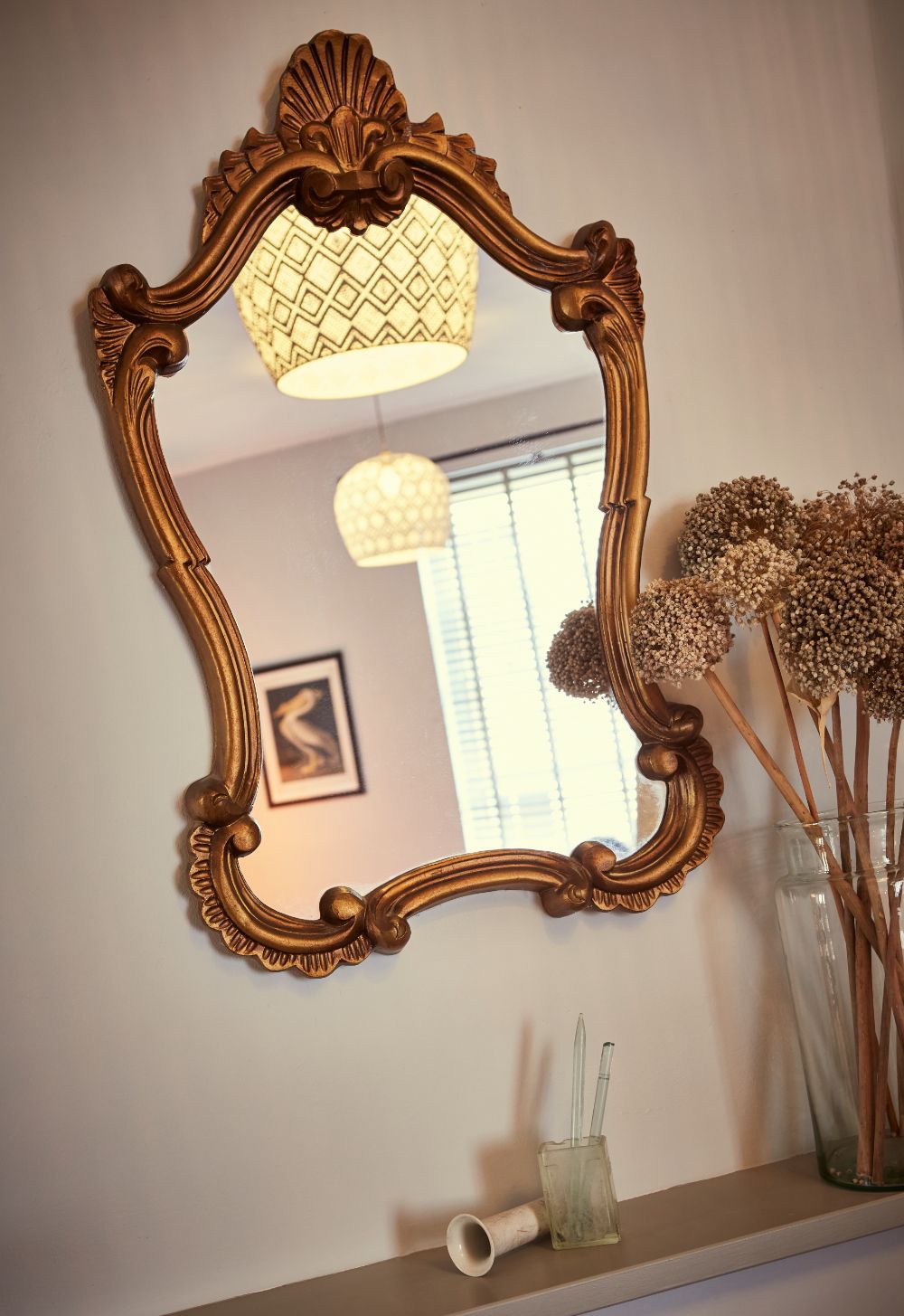 The ornate bedroom mirror reflecting natural light from the window, with dried flowers below