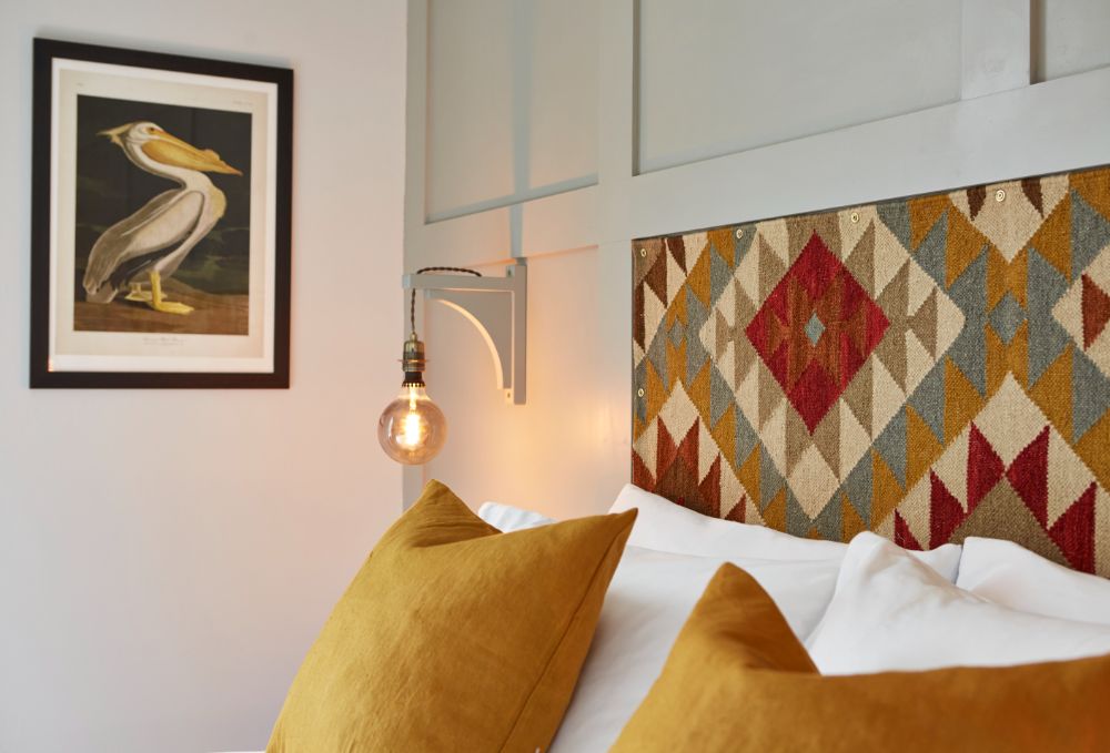 The pillows on the bed, with a tapestry headboard and quirky bedside light