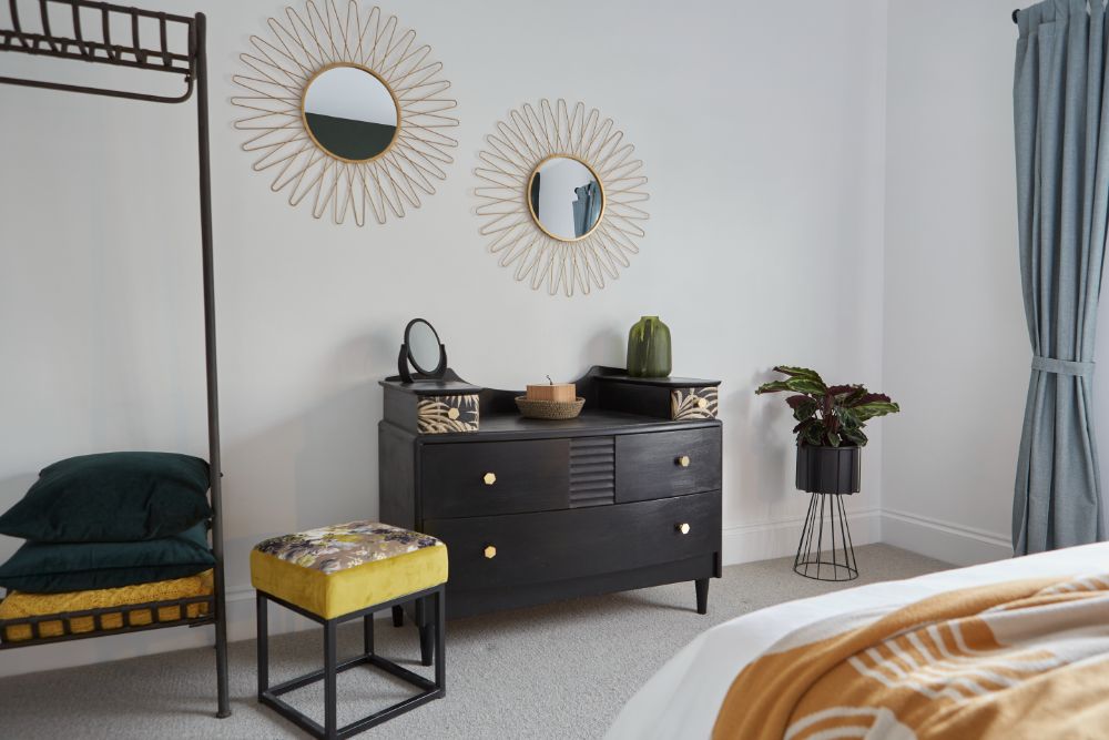 A view from the end of the bed to the bedroom mirrors and chest of drawers