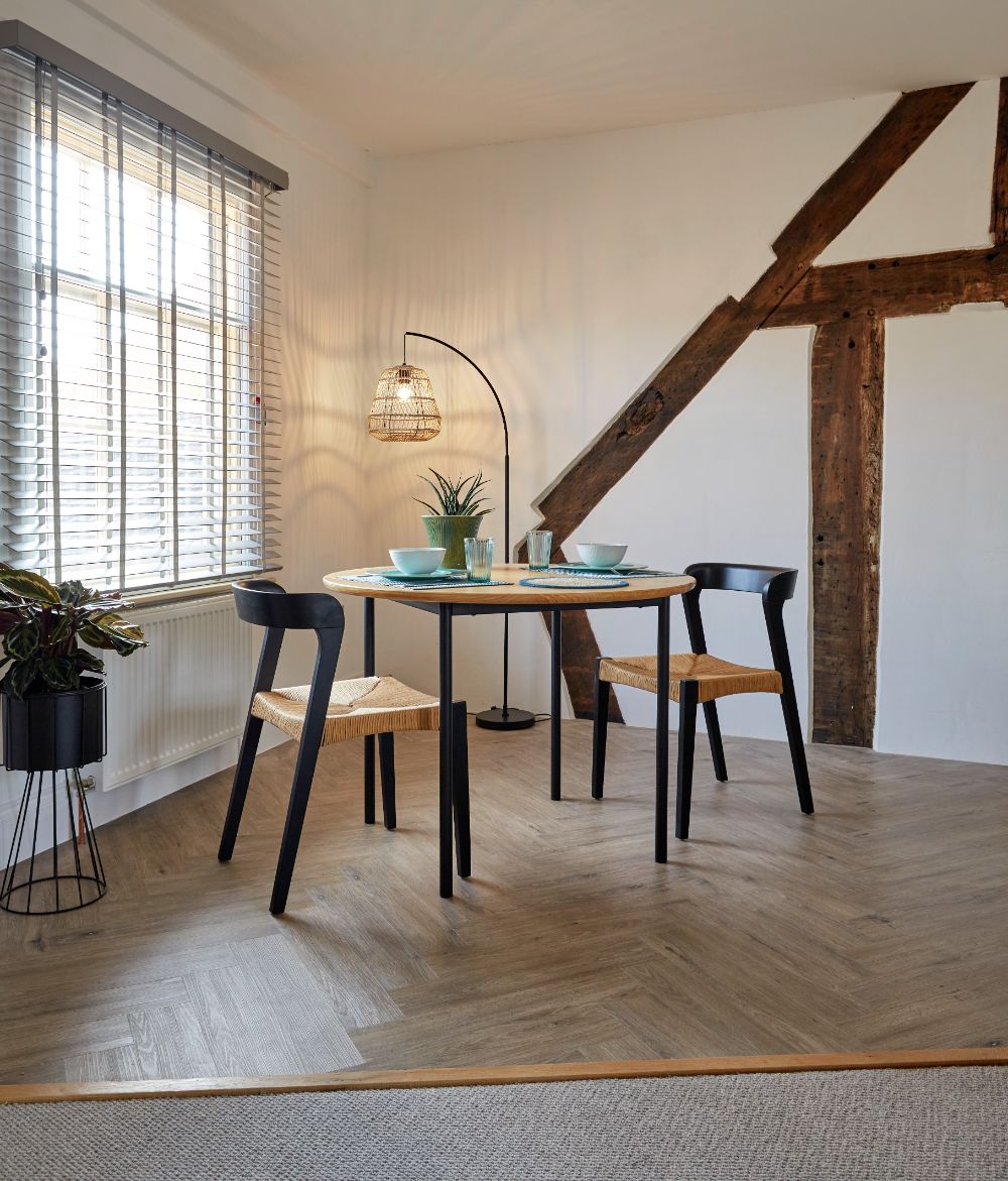 The dining table beside the kitchen window, with light flooding in and oak beams behind